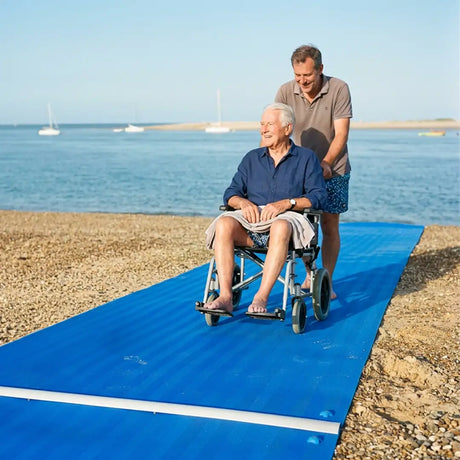 Usuario pasando con silla de ruedas por pasarela de playa resistente al agua salada y a los rayos UV para una mayor durabilidad dortomedical